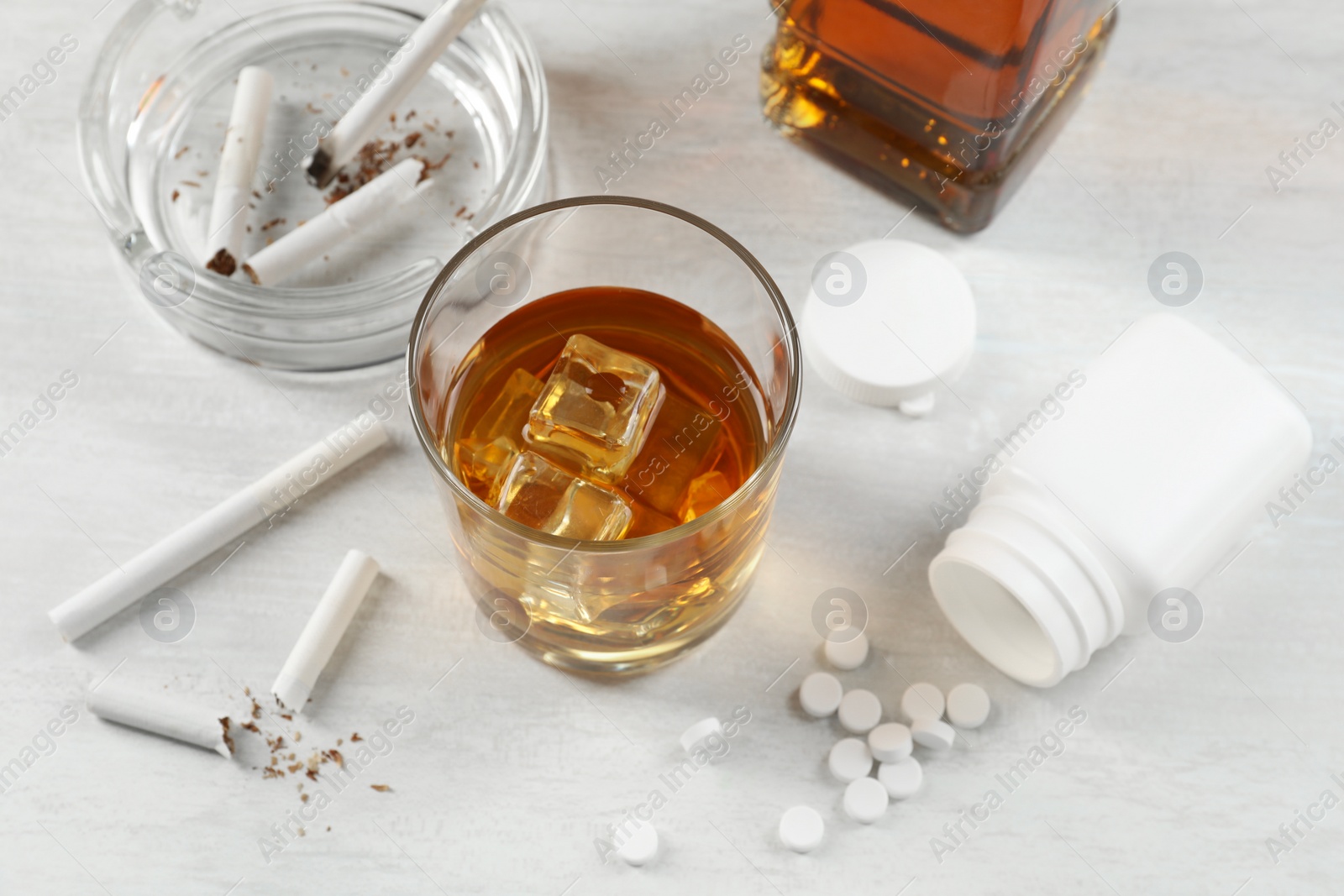 Photo of Alcohol and drug addiction. Whiskey in glass, cigarettes and pills on white table