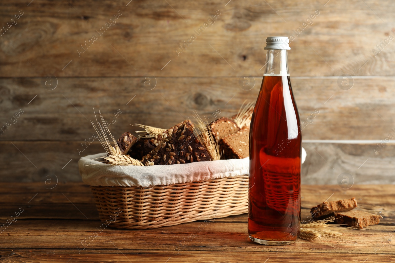 Photo of Bottle of delicious fresh kvass, spikelets and bread on wooden table