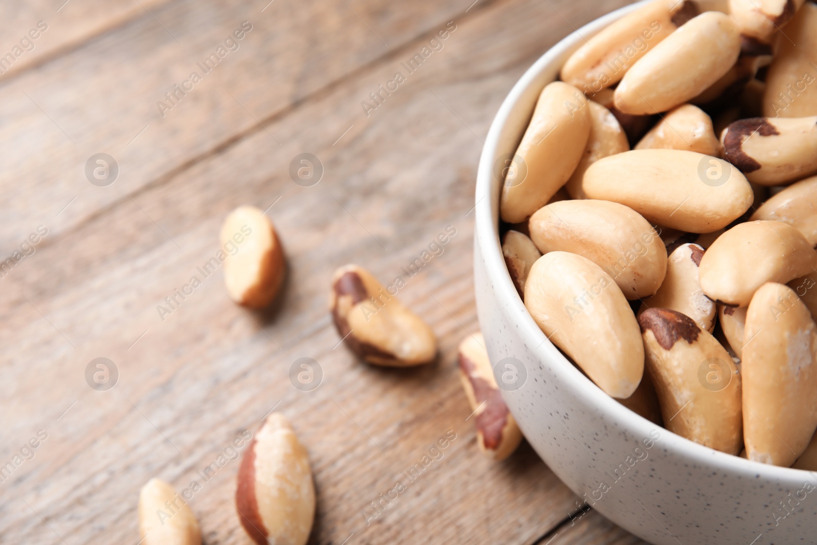 Photo of Bowl with tasty Brazil nuts on wooden table, closeup. Space for text