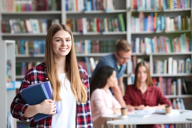 Photo of Young pretty woman with books in library. Space for text