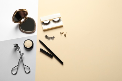 Flat lay composition with false eyelashes and other makeup products on color background, space for text