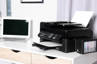 Photo of Modern printer with paper near laptop on white desk at home