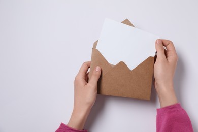 Woman taking card out of letter envelope at pink table, top view. Space for text