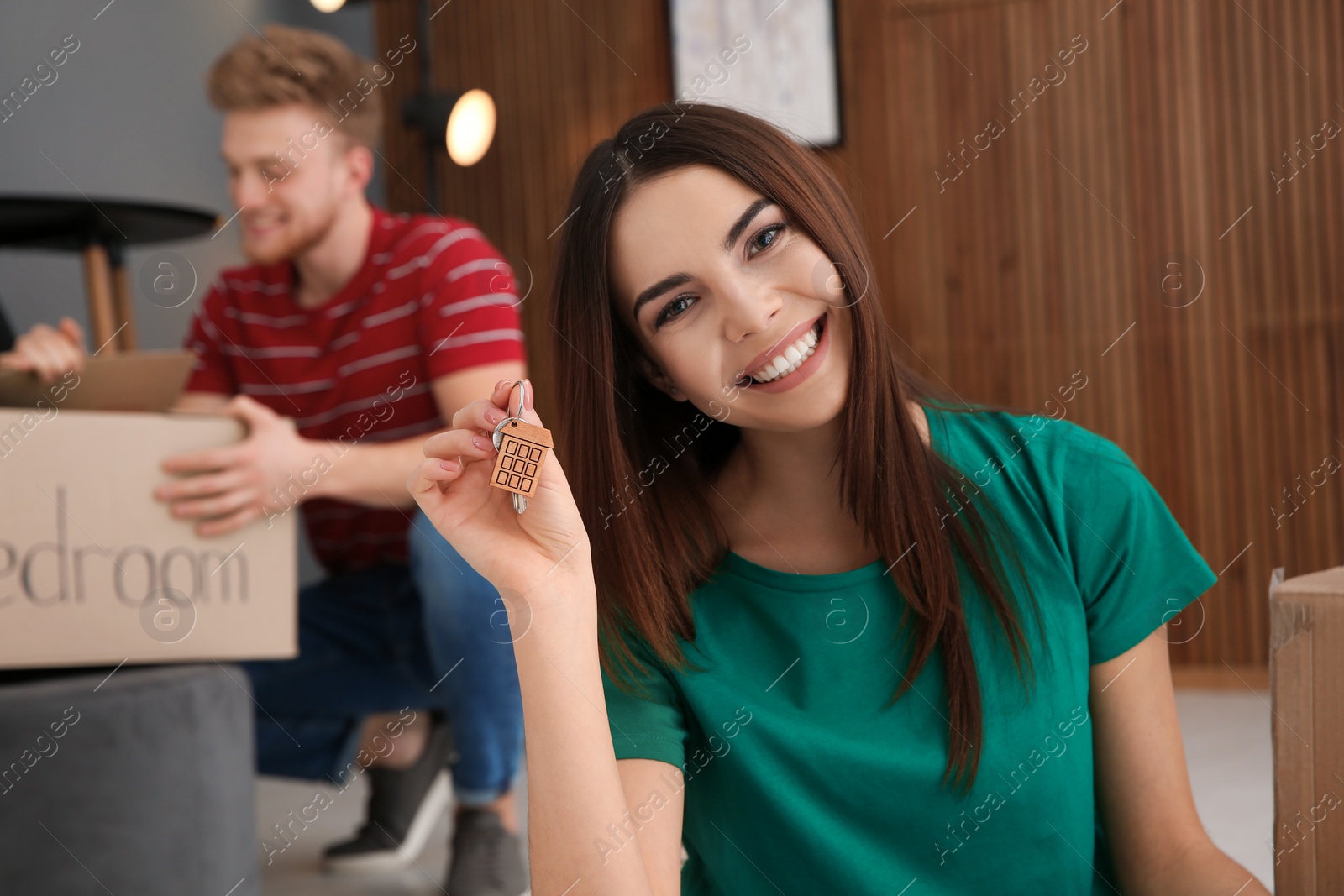 Photo of Young woman with key from new house and her boyfriend indoors. Moving day