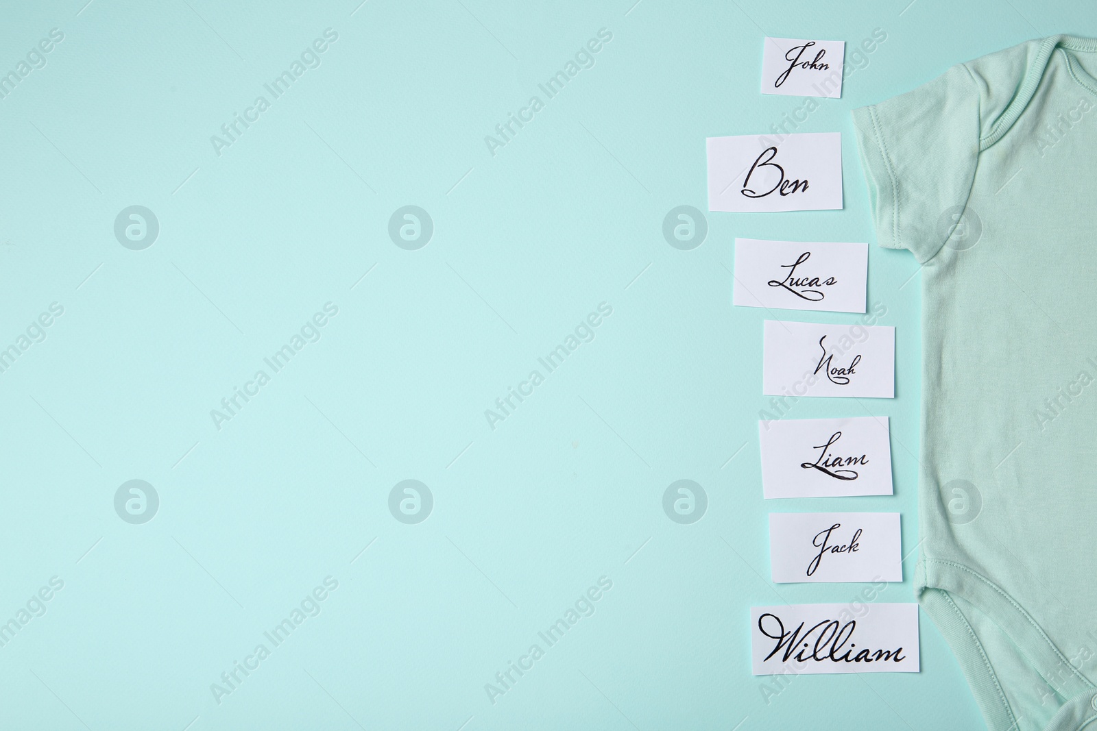 Photo of Paper sheets with written different baby names and bodysuit on light blue background, flat lay. Space for text