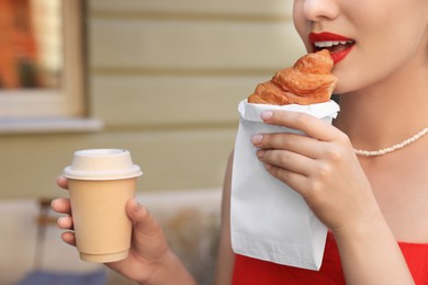 Photo of Woman eating croissant and paper cup of coffee outdoors, closeup