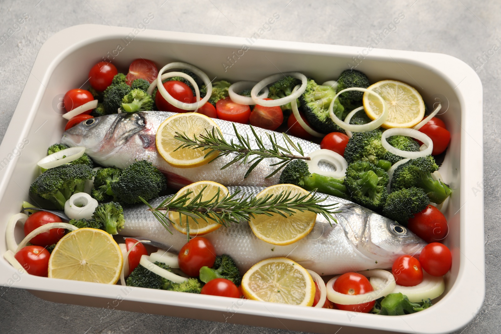 Photo of Raw fish with vegetables and lemon in baking dish on grey textured table