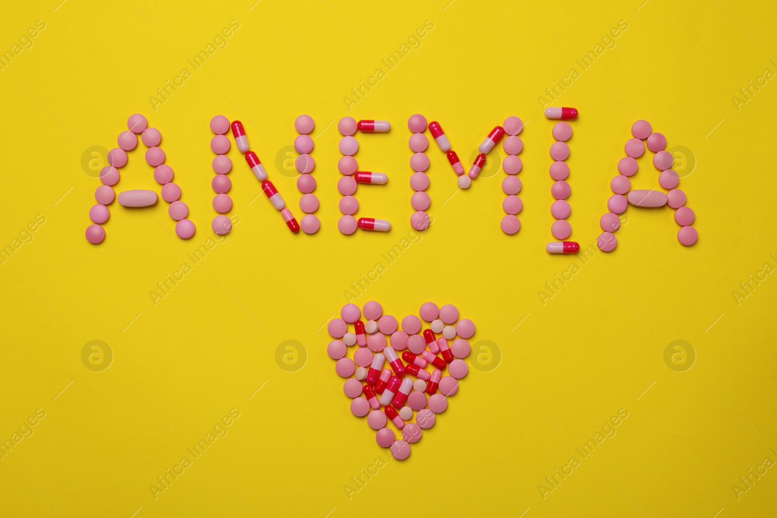 Photo of Word Anemia and heart made with pills on yellow background, flat lay