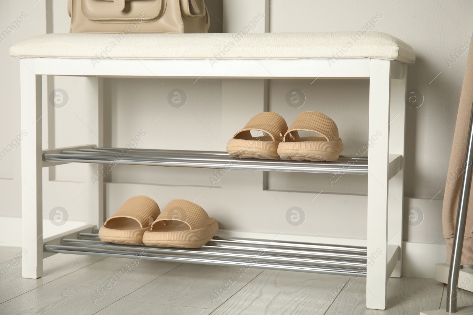 Photo of Storage bench with pairs of rubber slippers near white wall in room