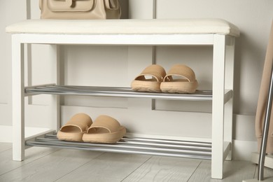 Storage bench with pairs of rubber slippers near white wall in room