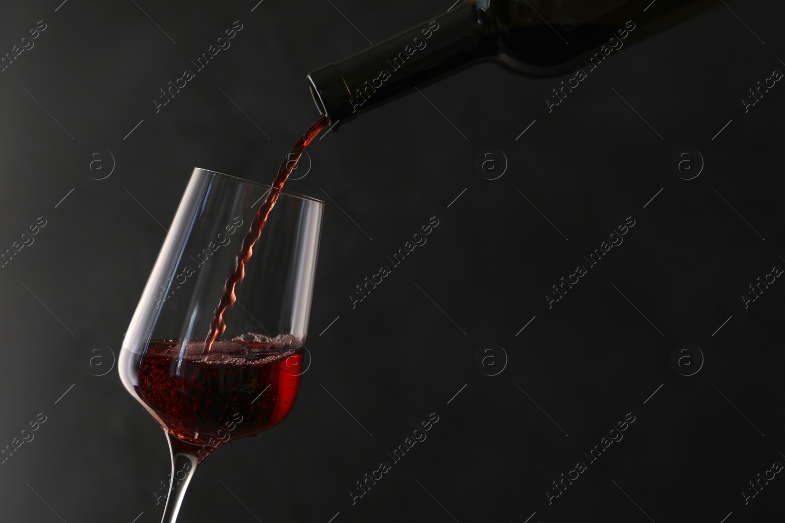 Photo of Pouring red wine from bottle into glass on dark background. Space for text