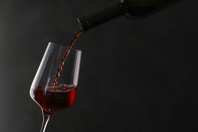 Photo of Pouring red wine from bottle into glass on dark background. Space for text