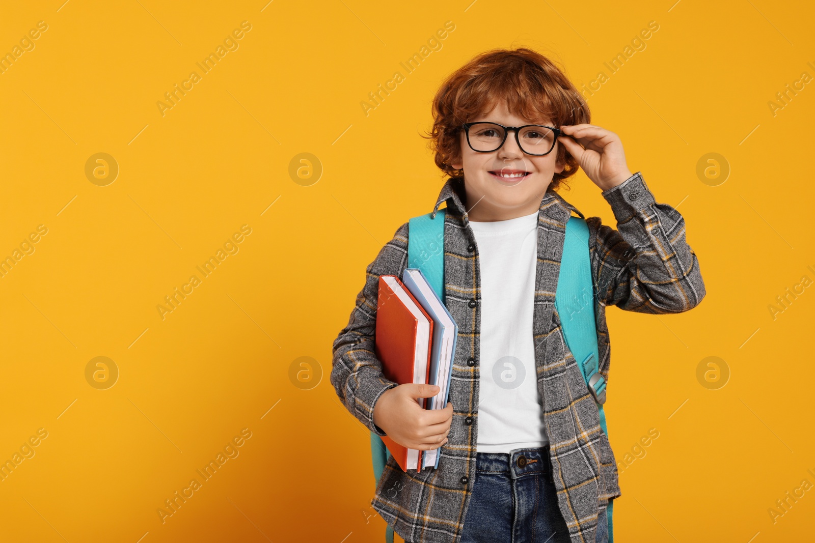 Photo of Happy schoolboy with backpack and books on orange background, space for text