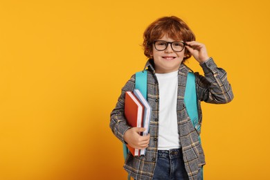 Photo of Happy schoolboy with backpack and books on orange background, space for text