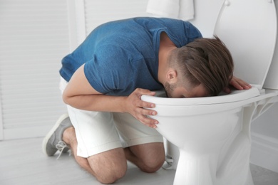 Young man vomiting in toilet bowl at home
