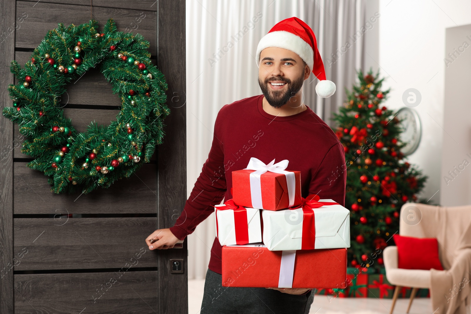 Photo of Young man in Santa hat with Christmas gift boxes received by mail indoors