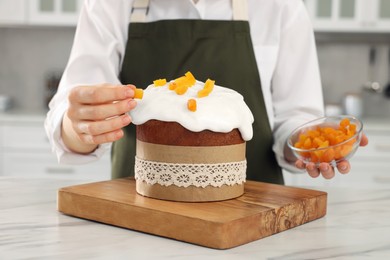 Woman decorating delicious Easter cake with dried apricots at white marble table in kitchen, closeup