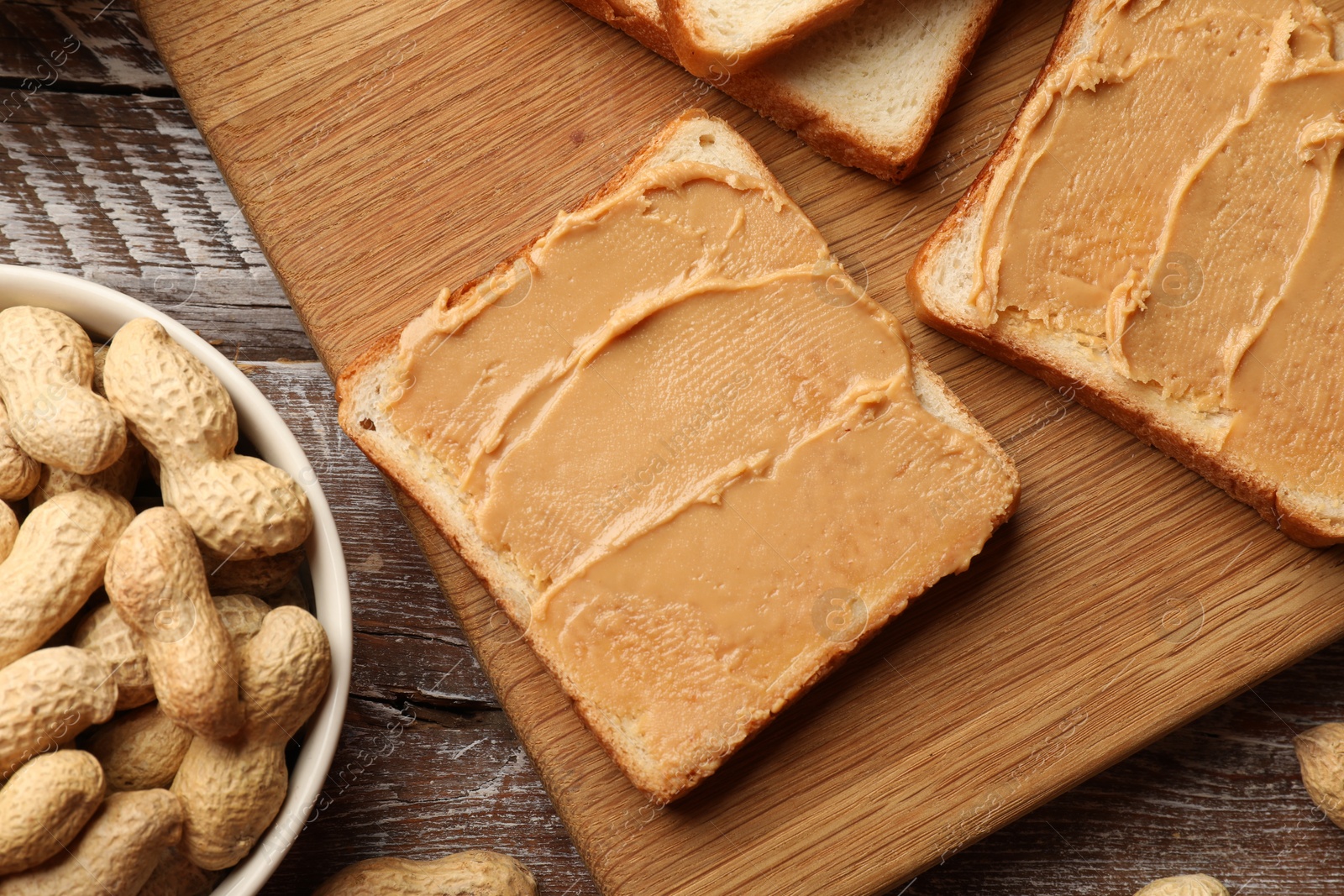 Photo of Tasty peanut butter sandwiches and peanuts on wooden table, flat lay