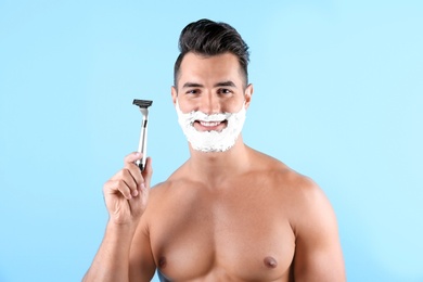 Photo of Handsome young man with shaving foam and razor on color background