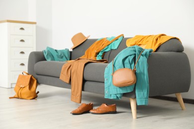 Photo of Messy pile of clothes on sofa and shoes in living room