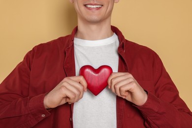 Happy volunteer holding red heart with hands on beige background, closeup