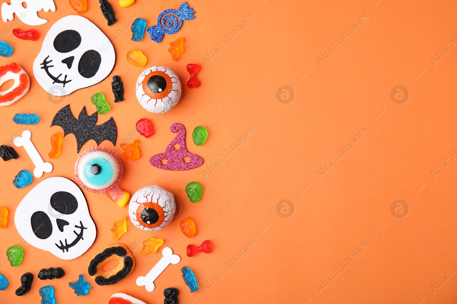 Photo of Tasty candies and Halloween decorations on orange background, flat lay. Space for text