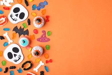 Tasty candies and Halloween decorations on orange background, flat lay. Space for text