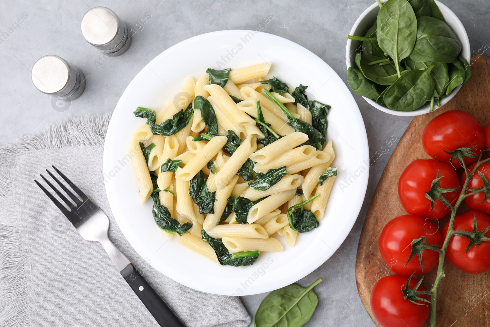 Photo of Tasty pasta with spinach and sauce served on grey textured table, flat lay