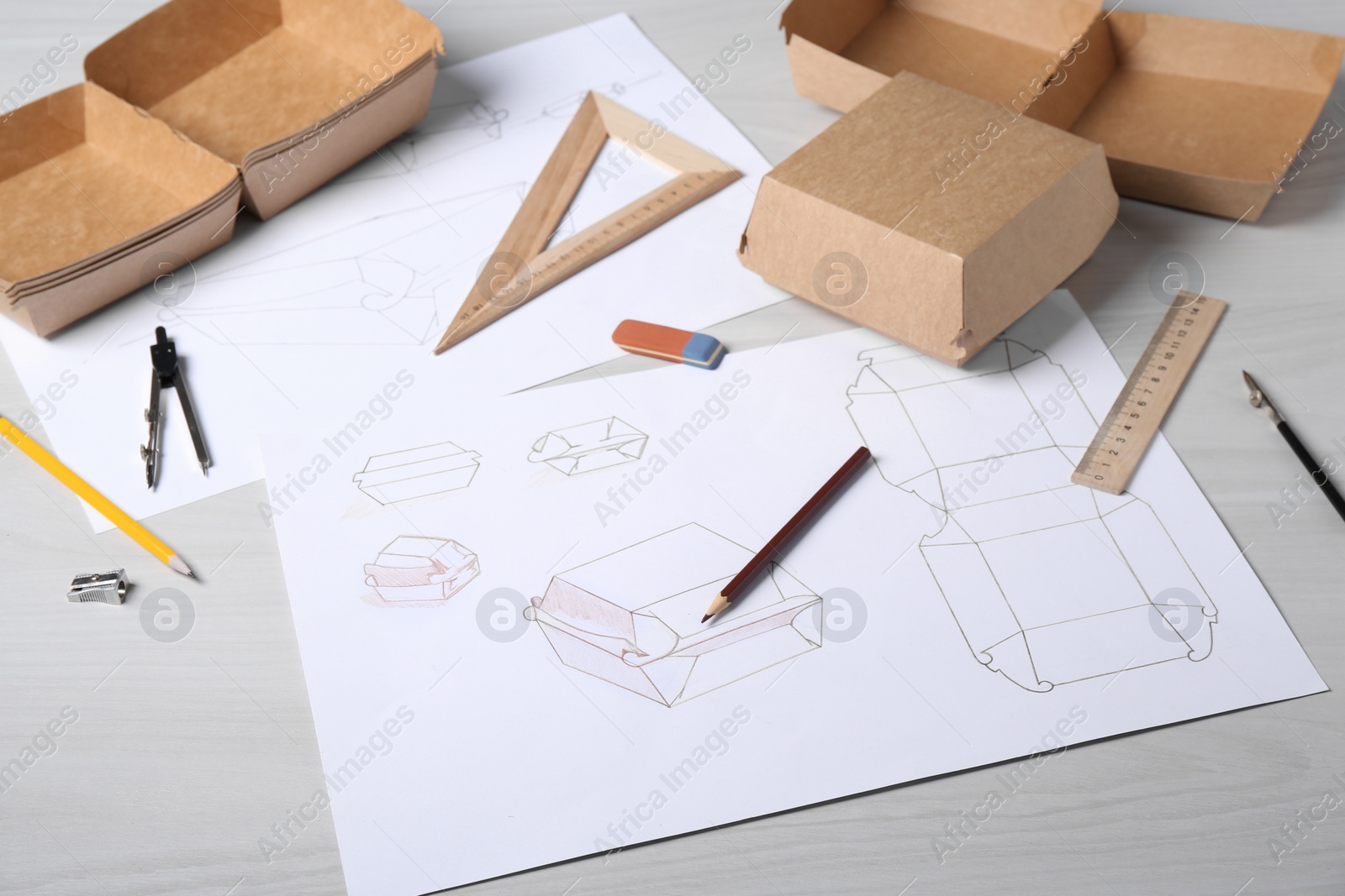 Photo of Creating packaging design. Drawings, boxes and stationery on light wooden table, closeup