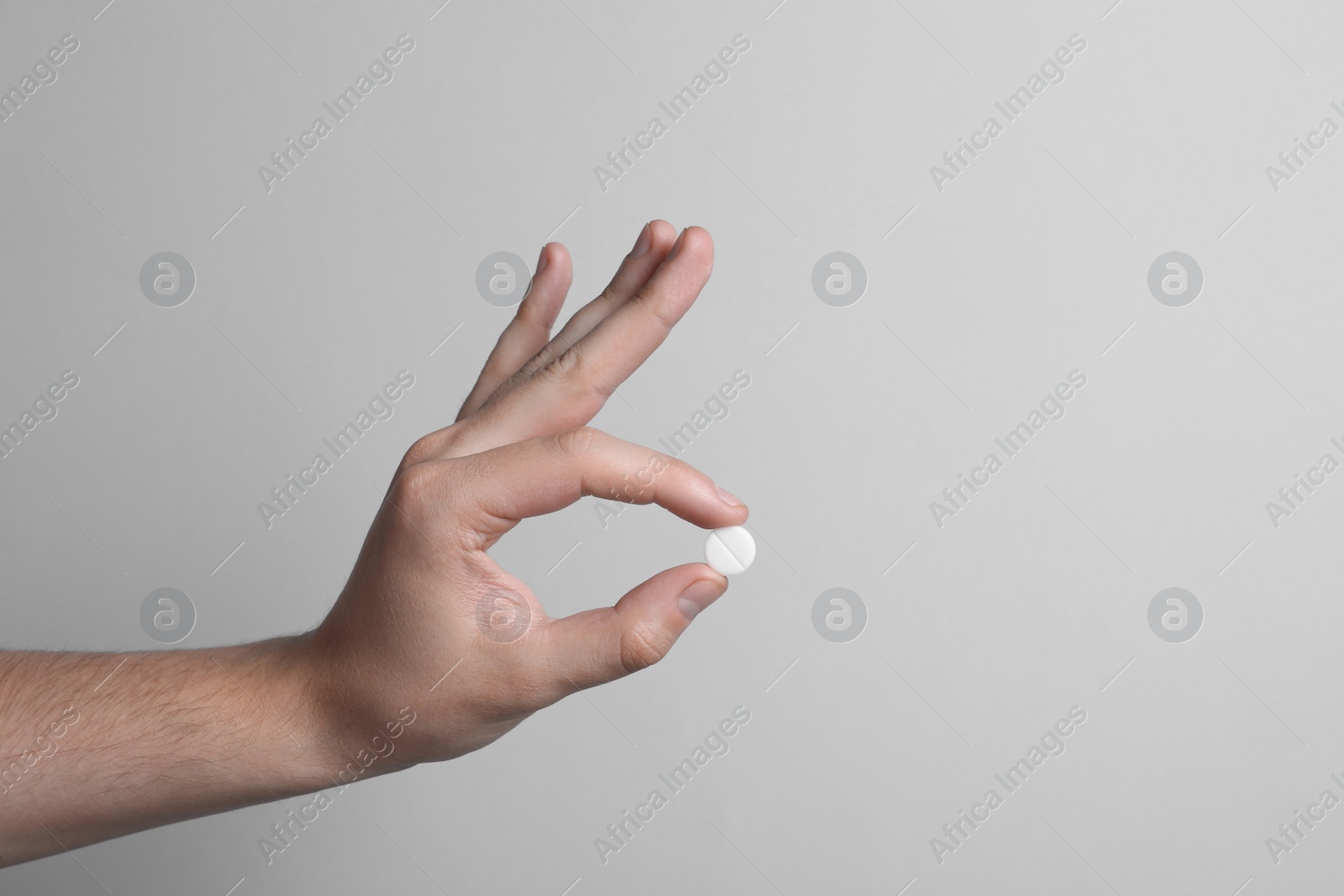 Photo of Man holding pill on light grey background, closeup. Space for text