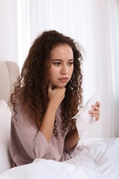 Sick African American woman with tissue in bed at home