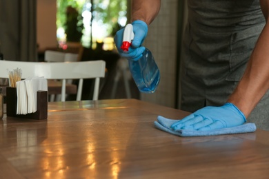 Waiter in gloves disinfecting table at cafe, closeup
