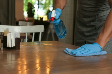 Photo of Waiter in gloves disinfecting table at cafe, closeup