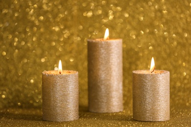 Stylish burning candles on gold shining background