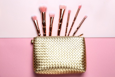 Bag with different makeup brushes on color background, flat lay