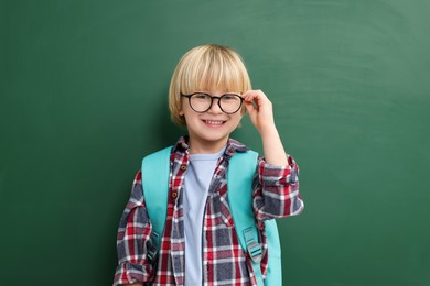 Photo of Happy little school child with backpack near chalkboard