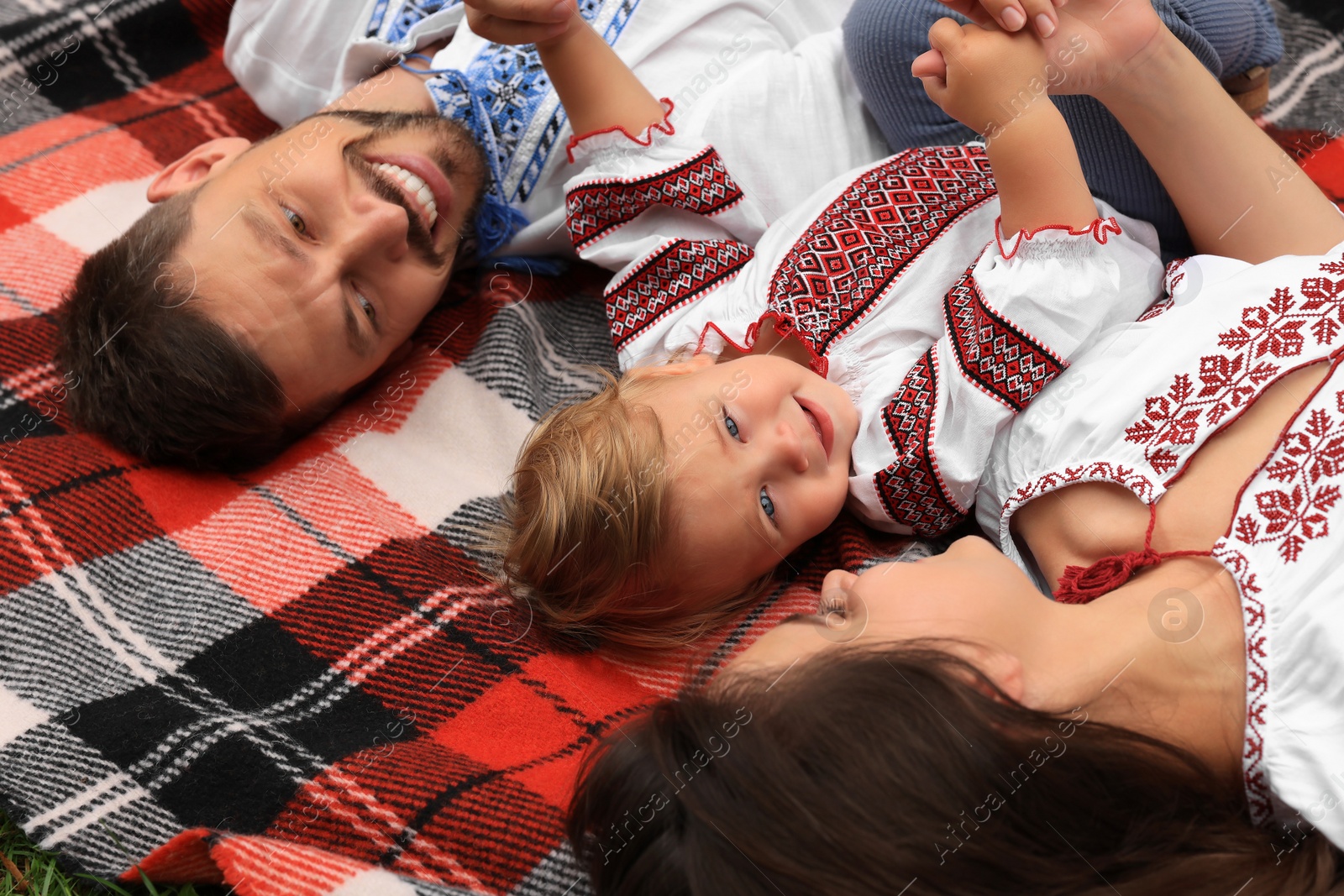 Photo of Happy family in national clothes lying on blanket together, closeup