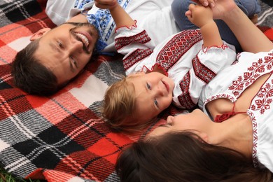 Photo of Happy family in national clothes lying on blanket together, closeup