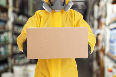 Man wearing chemical protective suit with cardboard box in store, closeup. Wholesale market 