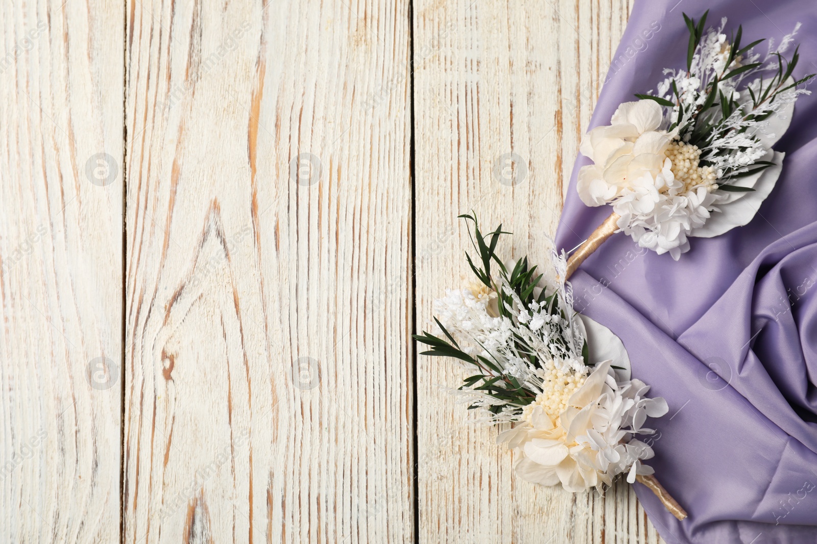 Photo of Stylish boutonnieres and purple fabric on light wooden table, top view. Space for text