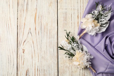 Photo of Stylish boutonnieres and purple fabric on light wooden table, top view. Space for text