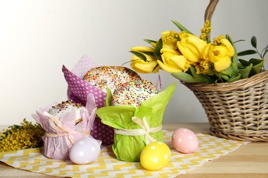 Photo of Delicious Easter cakes, dyed eggs and basket with flowers on wooden table