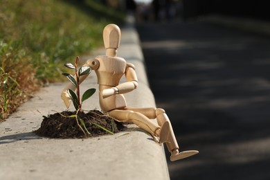 Photo of Wooden human figure with soil and green seedling outdoors, space for text