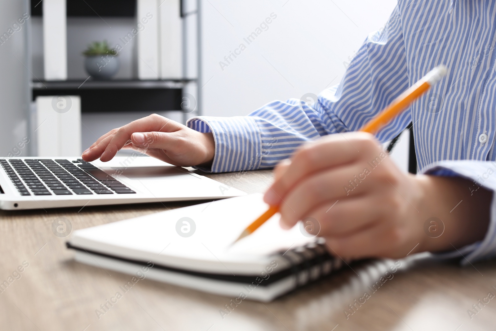 Photo of Woman with notebook working on laptop at wooden table in office, closeup