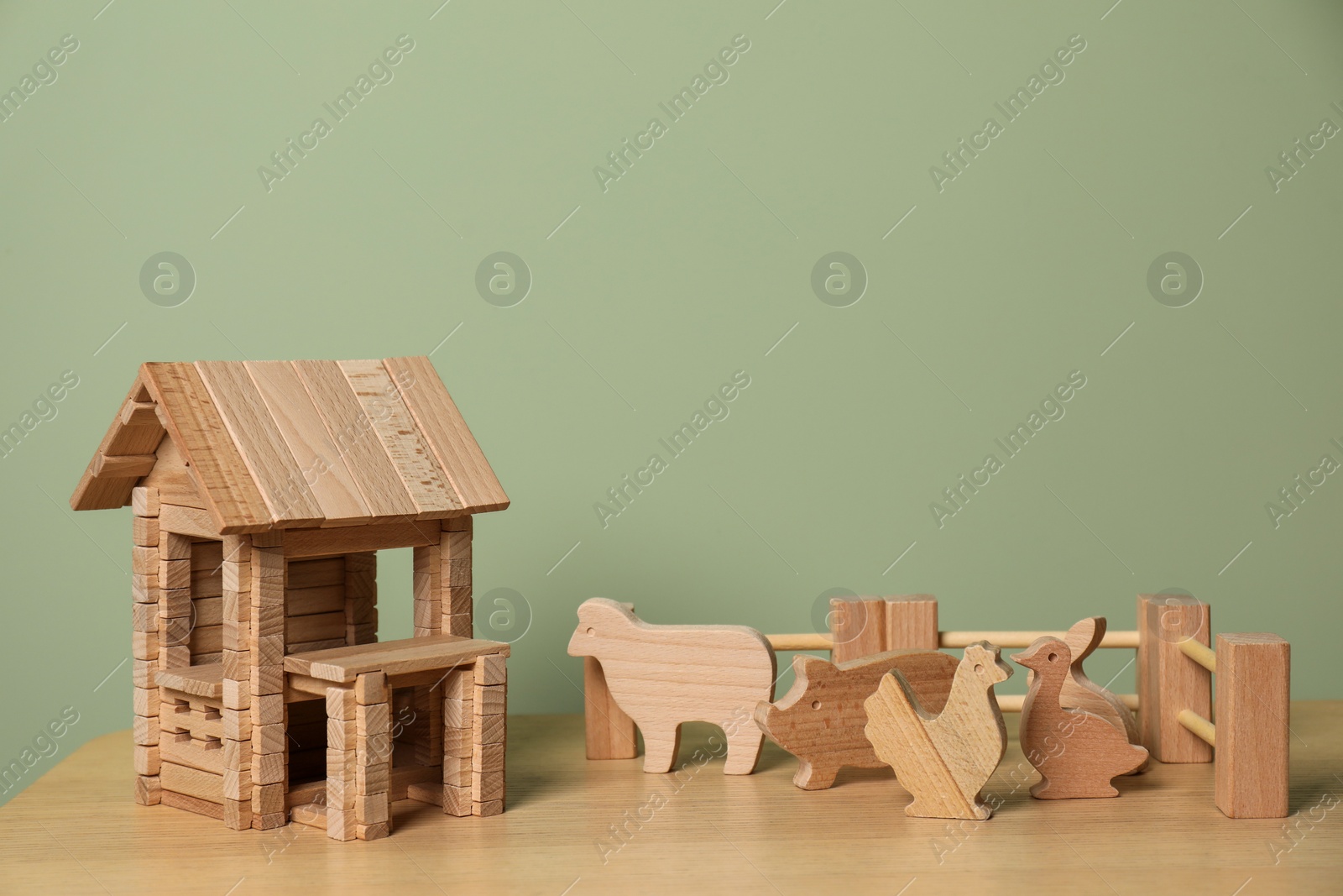 Photo of Wooden house, animals and fence on table near olive wall, space for text. Children's toys