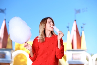 Photo of Young cheerful woman having fun with  cotton candy in amusement park