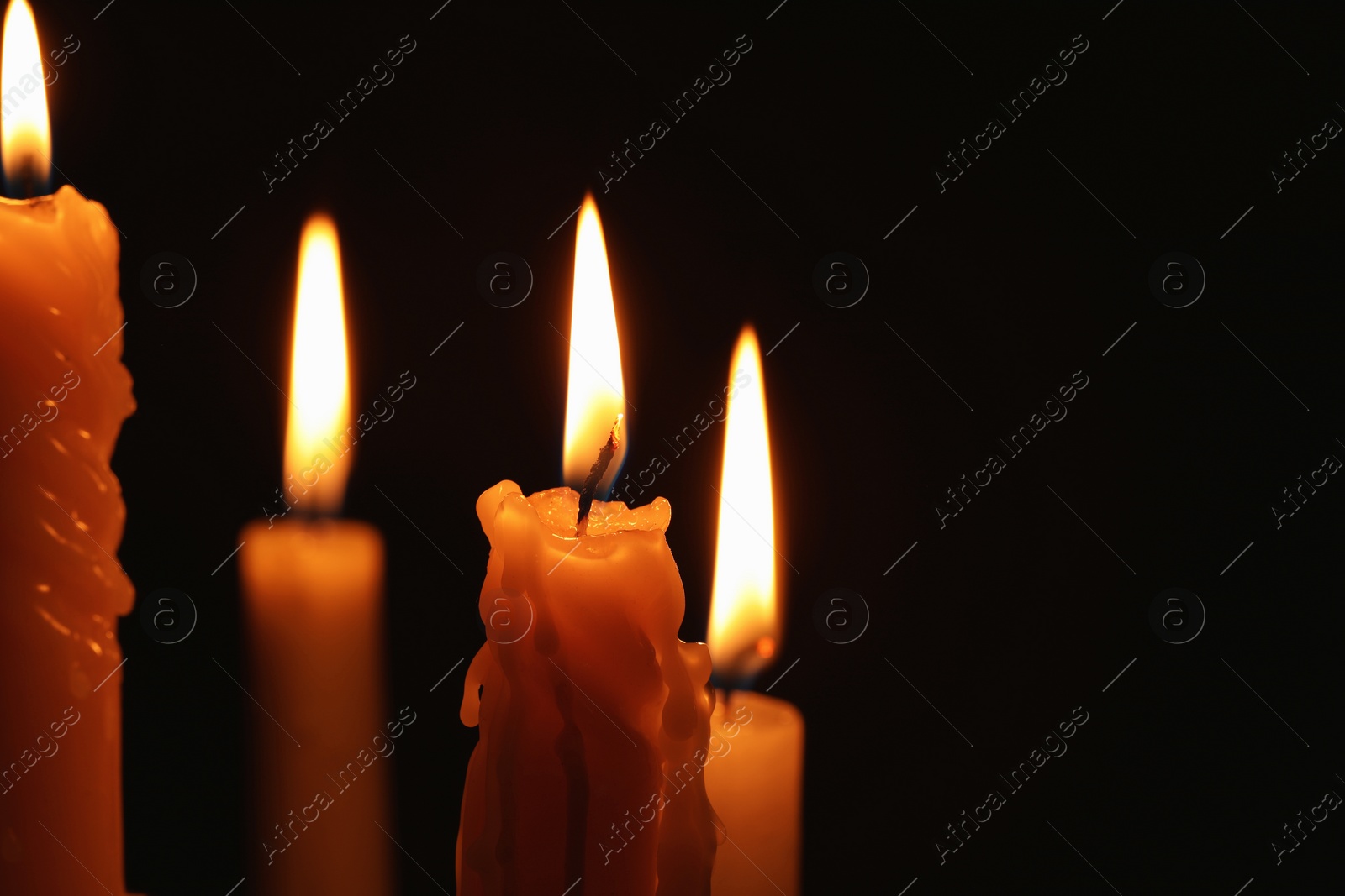 Photo of Burning candles on black background, closeup. Space for text