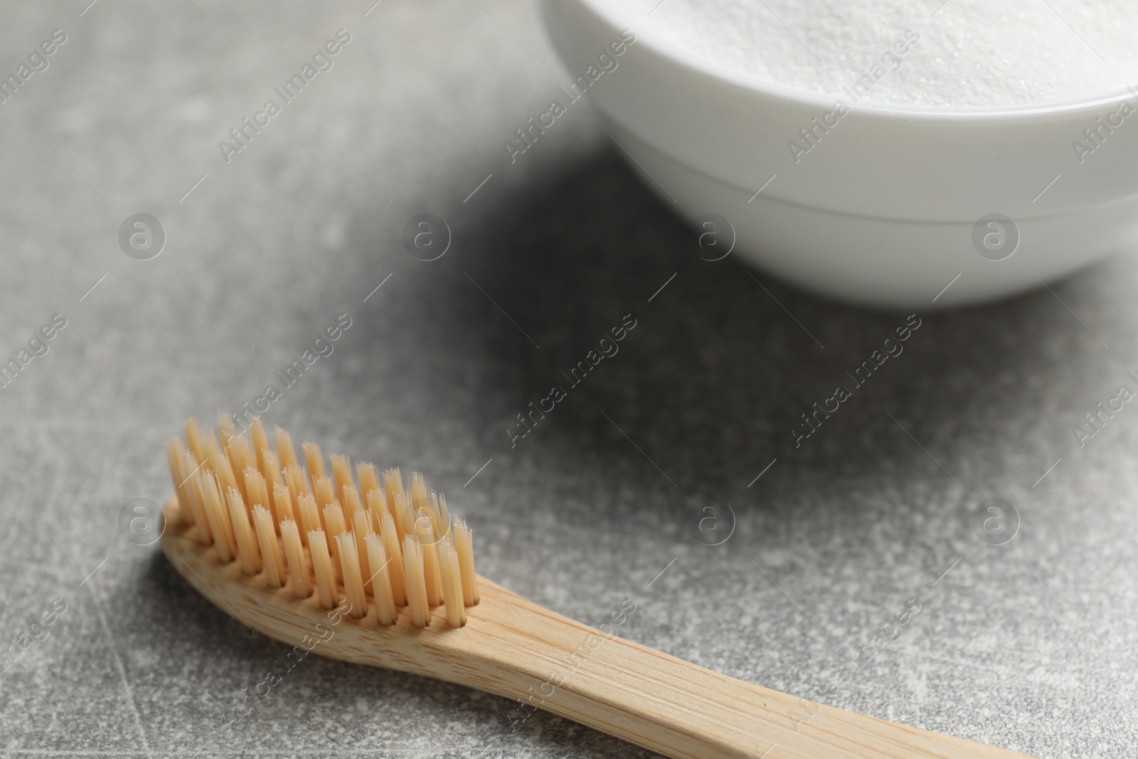 Photo of Bamboo toothbrush and bowl of baking soda on grey table, closeup