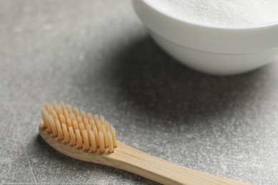 Bamboo toothbrush and bowl of baking soda on grey table, closeup