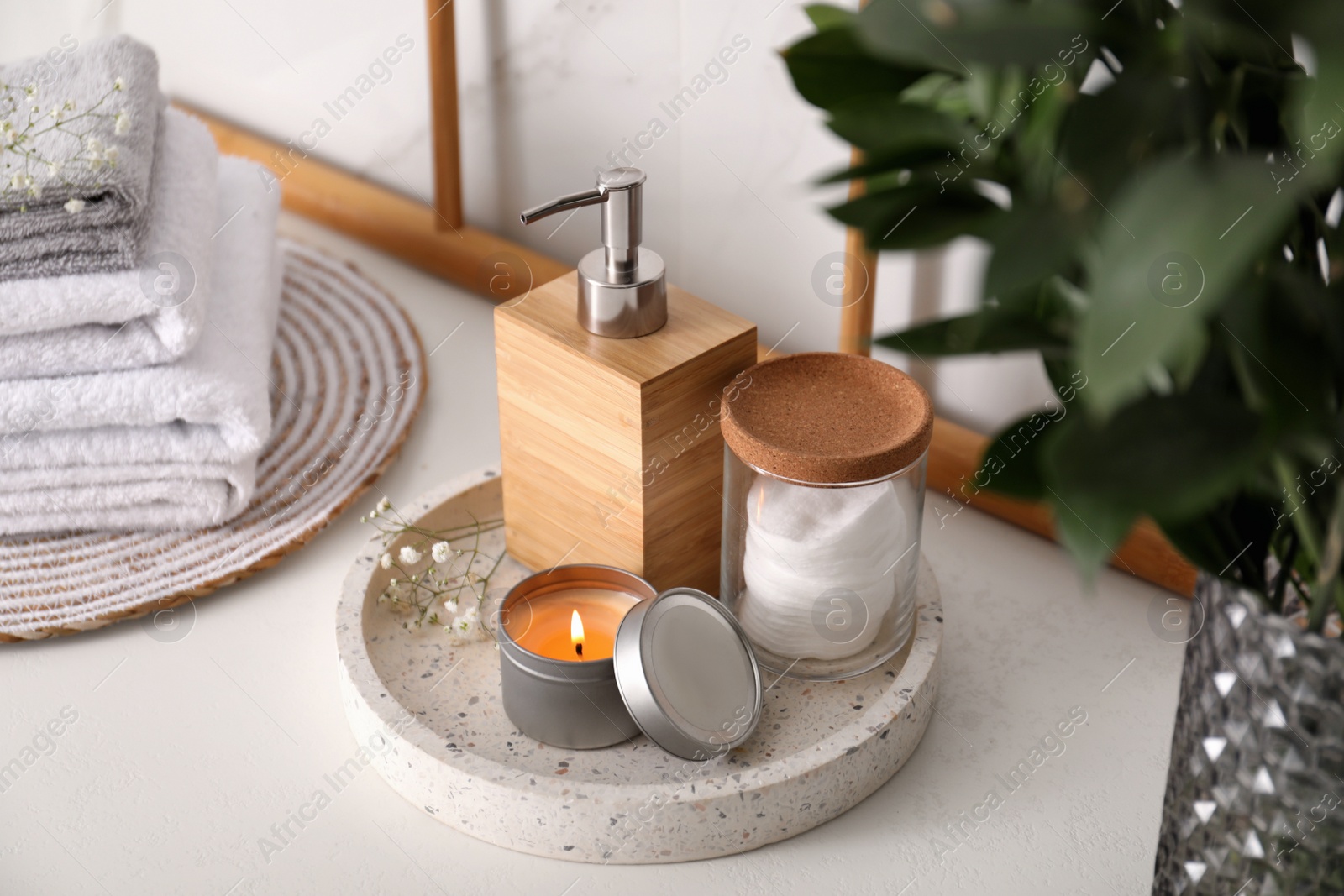 Photo of Tray with soap dispenser, cotton pads and burning candle on countertop in bathroom